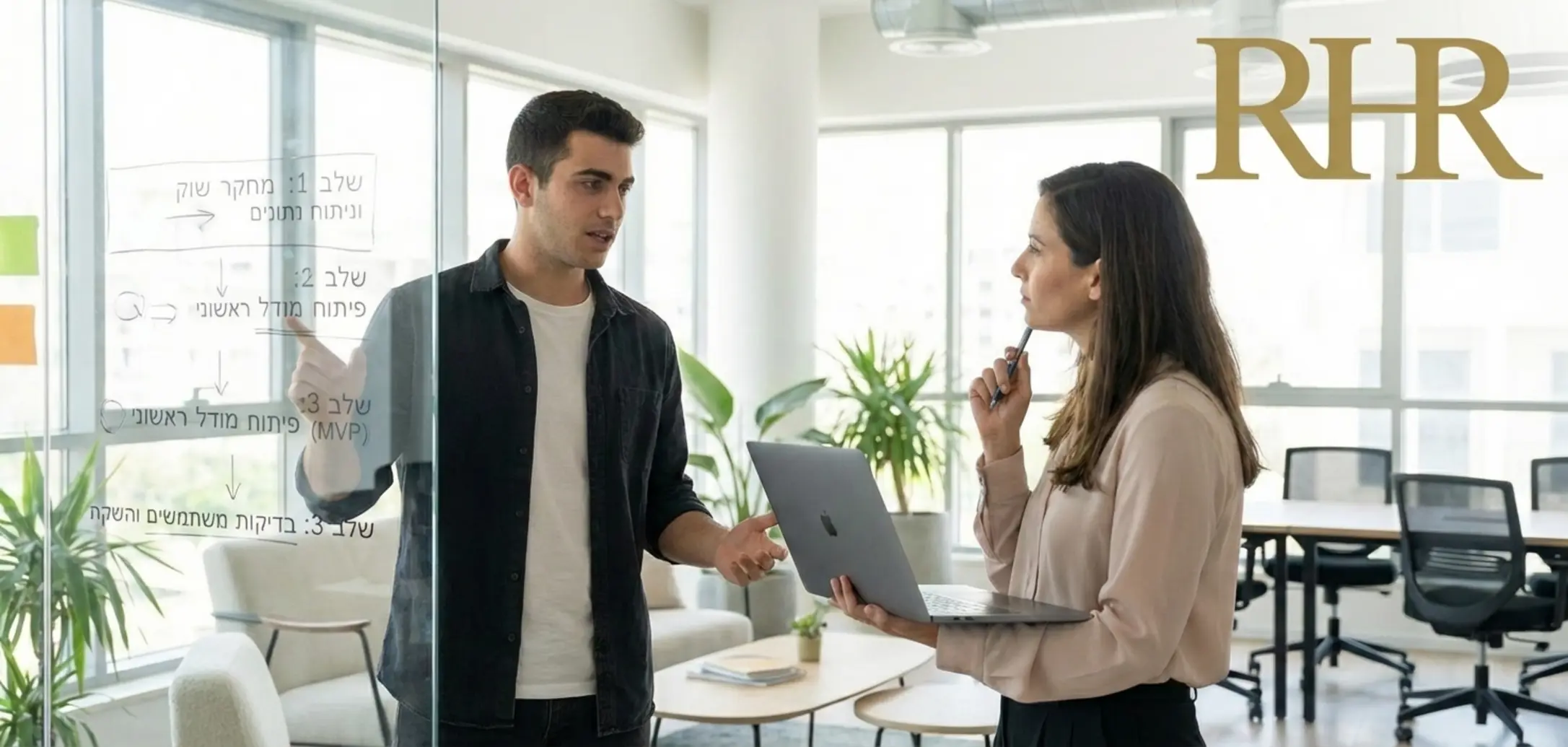 תמונה של מרואיין צעיר יושב מול מראיינת במשרד מודרני מואר היטב, המראיינת מעיינת במחשב נייד והמרואיין מסביר פרויקט על גבי לוח מחיק שקוף